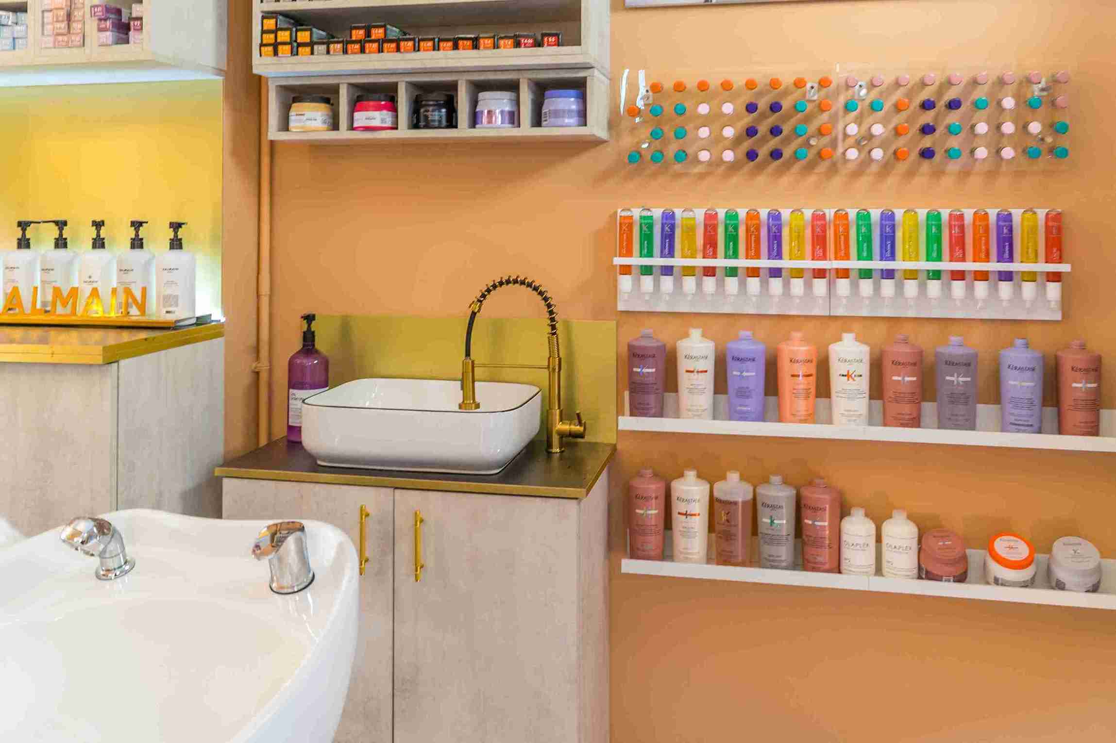Modern shampoo area featuring a white sink, gold faucet, and a display of colorful hair care products.